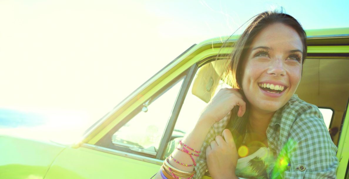 Smiling young woman sitting in a car parked overlooking a sea view